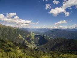 Panorama des grünen Tals und der Berge Panoramaansicht eines grünen Tals umgeben von Bergen, mit blauem Himmel und weißen Wolken.