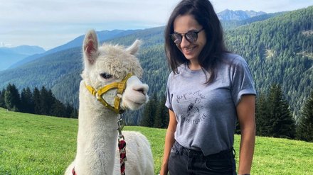 Mädchen mit Lama in den Bergen Mädchen steht neben einer Lama auf einer Wiese mit Bergblick.