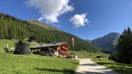 Almhütte in den Bergen Almhütte auf einer grünen Wiese mit Blick auf die Berge und den blauen Himmel.